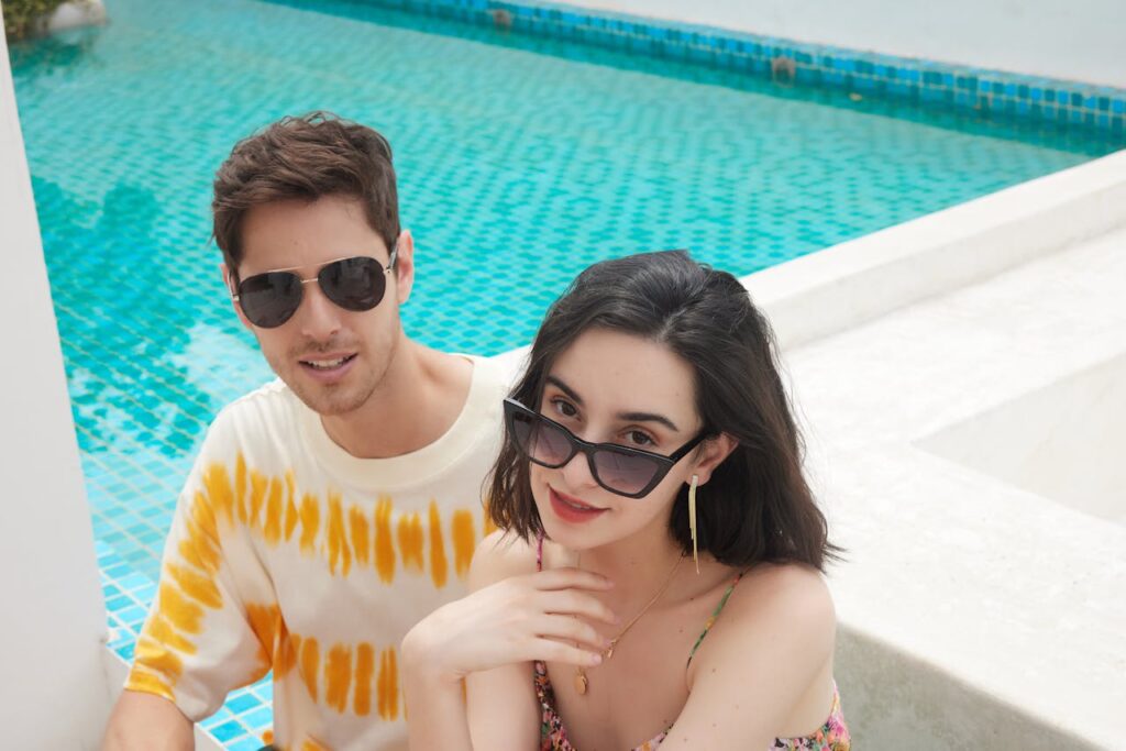 A fashionable couple enjoying a sunny day by the pool, wearing stylish sunglasses.