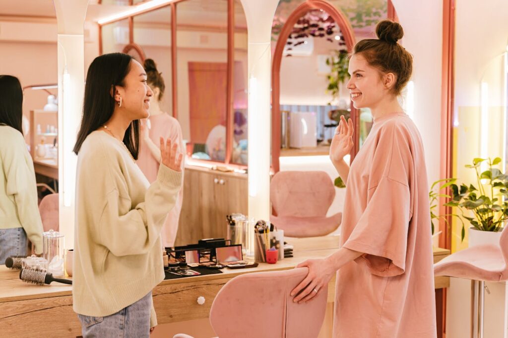 Two friends share a joyful conversation inside a stylish, well-lit salon with beauty tools around.